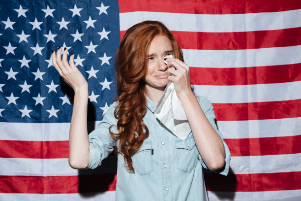 istock Sad redhead young lady cry over USA flag. Looking aside. 1392587639