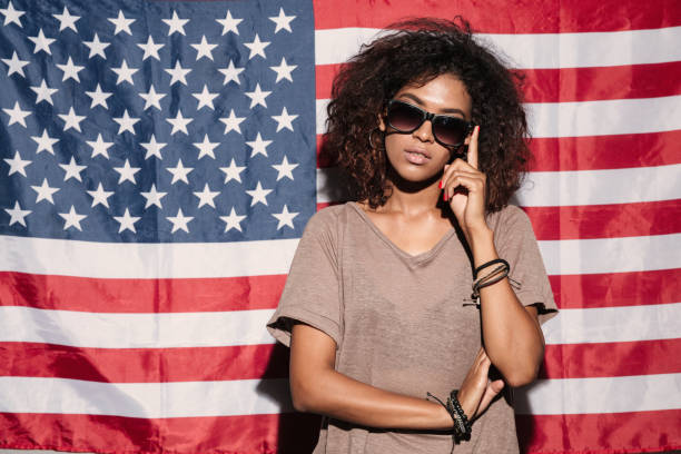 istock Serious african young lady standing over USA flag 1392587785