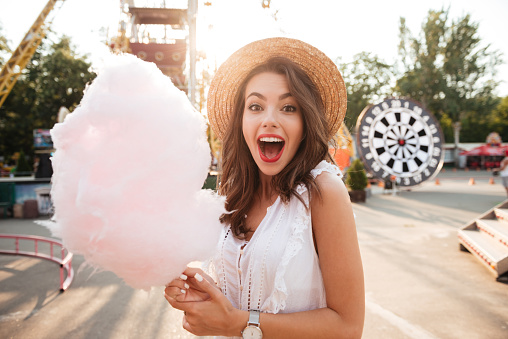 Close up portrait of a smiling excited girl holding cotton candy at amusement park