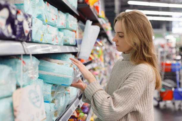 Young woman mother chooses diapers at supermarket in shop mall. Hygiene products for children stock photo