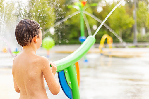 Little boy having fun at playground. Summer fun at the water park. Children at water playground of urban amusement park.