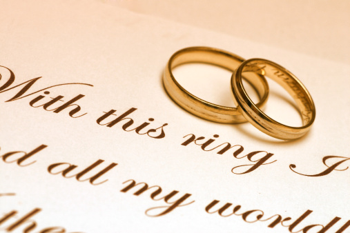 Two wedding ring laying on a paper with text of wedding vow.