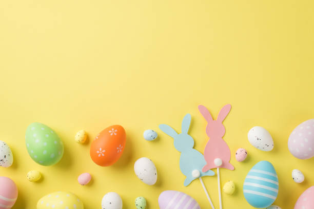 istock Top view of multicolored Easter eggs and quail ones with two rabbits on sticks situated on the isolated yellow background copyspace 1392598720