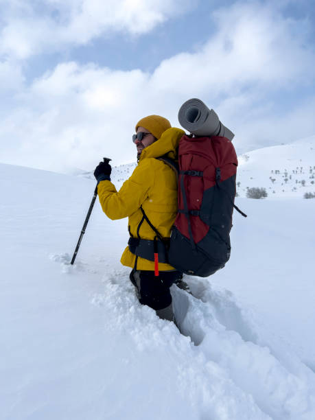 Man with backpack standing on snow-covered landscape, connecting using smartphone during a cold outdoor adventure