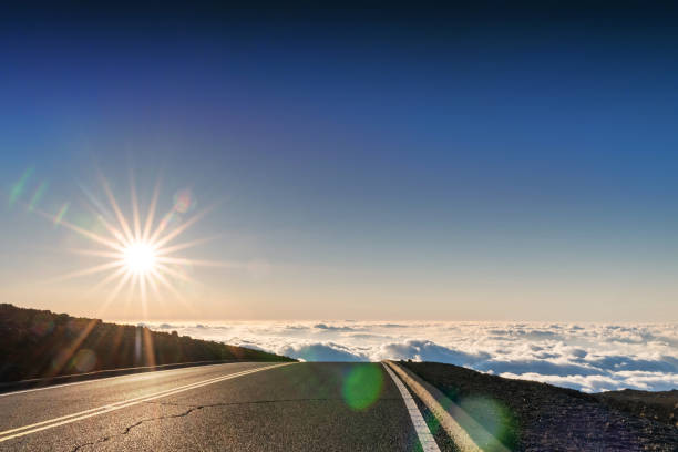 gepflasterte autobahn oben in großer höhe, über wolken, mit sonnenausbruch im hintergrund - haleakala national park maui nature volcano stock-fotos und bilder