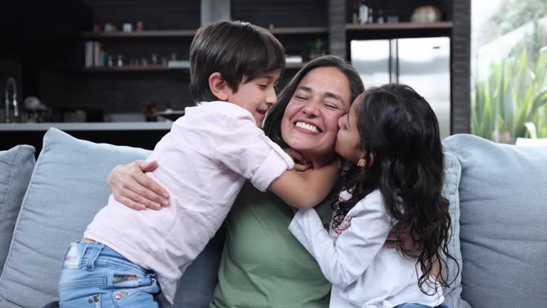 Loving mother hugging her son and daughter while they smile and kiss her on the cheek celebrating mother’s day - Lifestyles