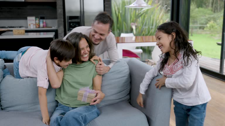 Happy woman texting on smartphone and loving kids and father surprising her with a mother’s day gift - Lifestyles and celebration concepts
