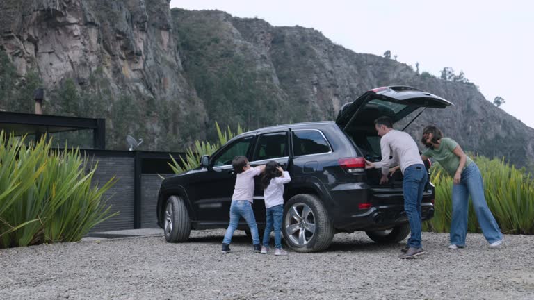 Happy family packing the bags in the trunk to their car ready for a road trip