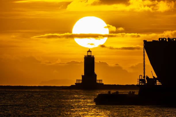 Lighthouse with rising Sun and Ship on right.