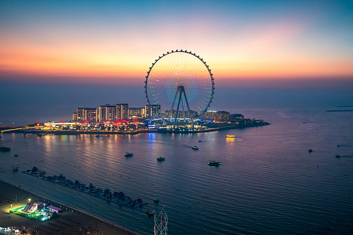 Bluewaters island leisure spot in Dubai with large Ferris wheel seen from JBR beach in Dubai Marina area at blue hour. United Arab Emirates travel destination