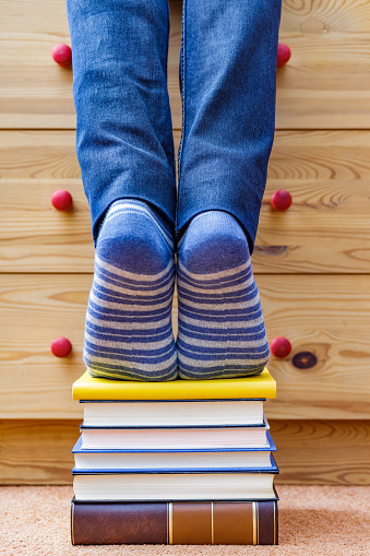 Madrid, Spain. April, 19 2022. Feet with socks on tiptoes on pile of books. Concept: Use books to achieve your goals