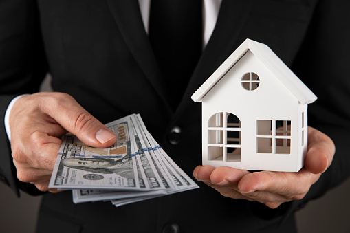 Man holding house model and Dollar bills