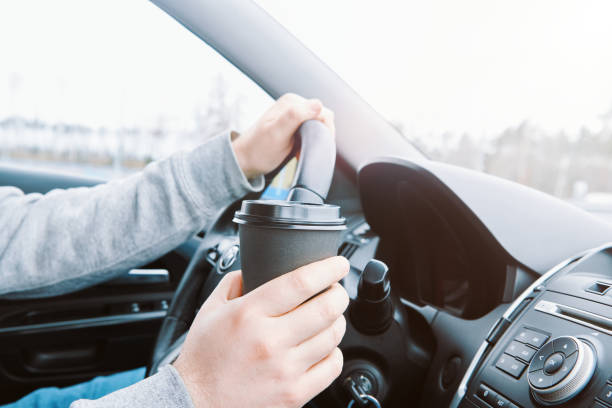 istock Man drinking coffee while driving the car. Driver holds Black paper cup in a car 1392605434