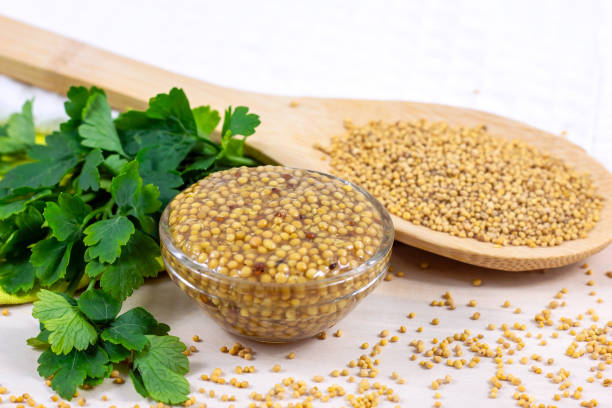 Yellow Dijon mustard sauce in glass dip with wooden spoon full of dry mustard seeds on the table in the kitchen Yellow Dijon mustard sauce in glass dip with wooden spoon full of dry mustard seeds on the table in the kitchen. dijonnaise stock pictures, royalty-free photos & images