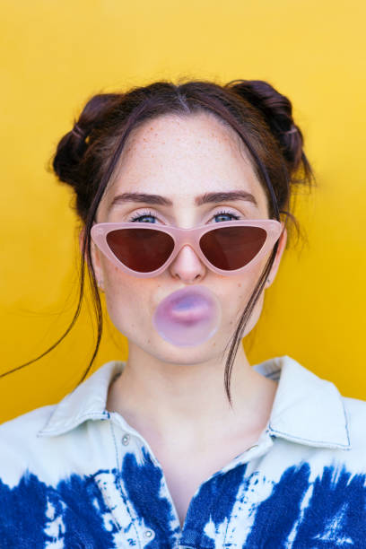 mujer soplando una burbuja de chicle sobre un fondo amarillo - chewing gum women bubble blowing fotografías e imágenes de stock