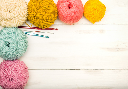 Balls of colored yarn and crochet hooks on light wooden background with copy space