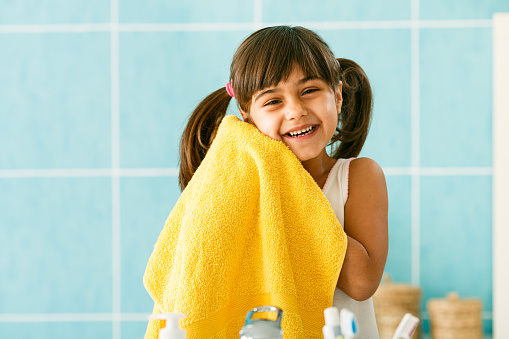 Little girl holding towel and smiling after washing her face as daily hygiene routine