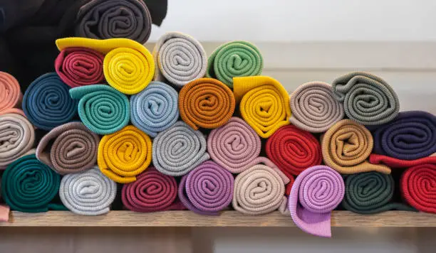 Multi-colored knitted fabrics rolled up in rolls lying on shelf of store or factory