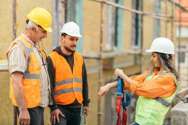 istock Female occupational safety specialist explaining  to construction site workers how to use  safety harness 1392612861