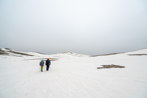 Alpinist climbers are walking on mountain crest on extreme harsh conditions with overcast sky before reaching the peak