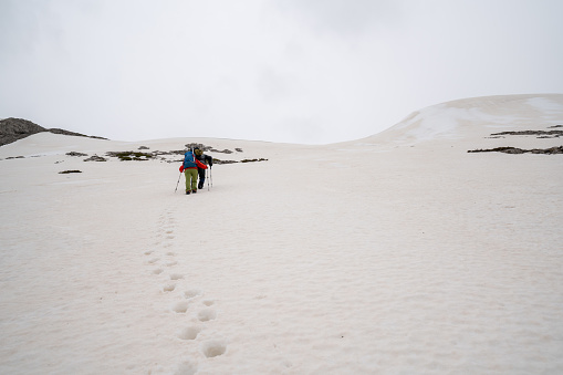Alpinist climbers are walking on mountain crest on extreme harsh conditions with overcast sky before reaching the peak