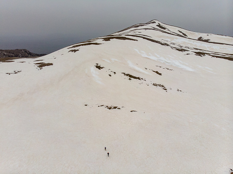 Alpinist climbers are walking on snow on mountain crest on extreme harsh conditions with overcast sky before reaching the peak