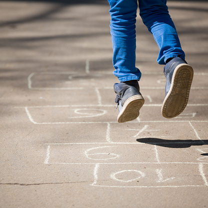 Closeup of the feet of a child playing hopscotch, painted on asphalt. Games for children in the fresh air. The concept of fun children's summer holidays.