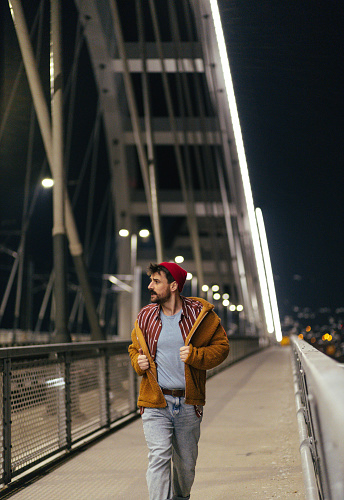 Young fashionable man walking on a bridge at night.