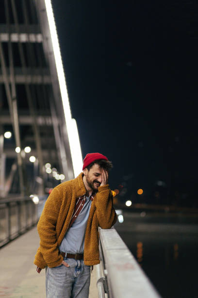 istock Young handsome fashionable man with a beard leaning on a bridge rail at night 1392614037