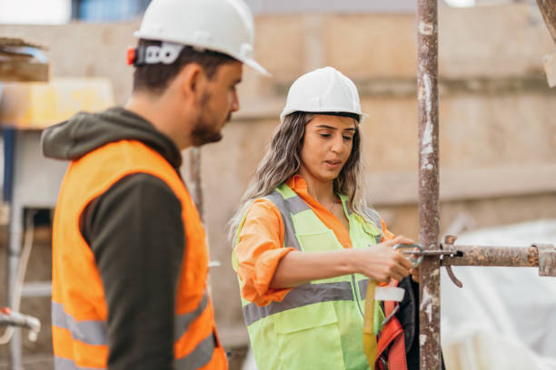 istock Female occupational safety specialist explaining  to construction site worker how to use  safety harness 1392614302