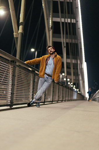 Young handsome fashionable man with a beard leaning on a bridge rail at night.
