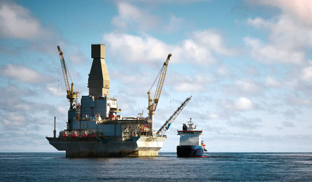 Oil rig offshore drilling platform and support vessel Oil rig offshore drilling platform and support vessel. Blue cloudy clear sky, sea surface power equipment stock pictures, royalty-free photos & images