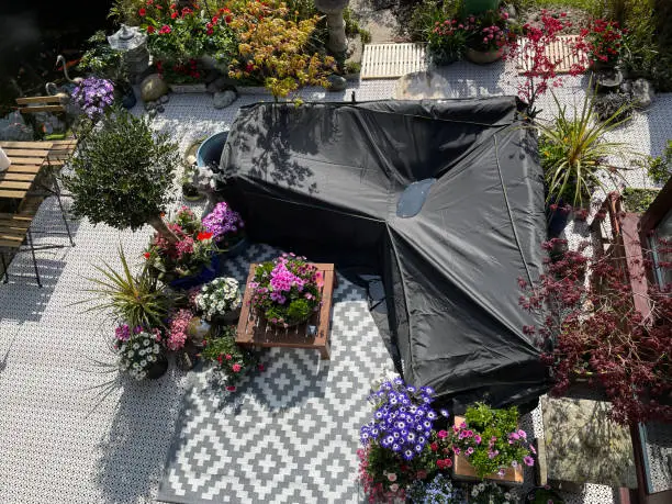 Photo of Close-up image of outdoor lounging area in Spring, puddled waterproof furniture cover protecting hardwood seating with cushions, wooden table top with flowering plant centrepiece, bonsai trees, Japanese maples, koi pond, landscaped oriental design garden,