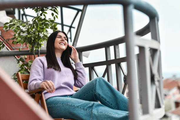 istock Smiling Female Beauty Talking On Phone While Sitting On Balcony Chair 1392624149