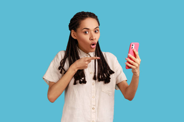 istock Woman with dreadlocks points at blank phone screen, amazed with its functions, advertises technology 1392624593