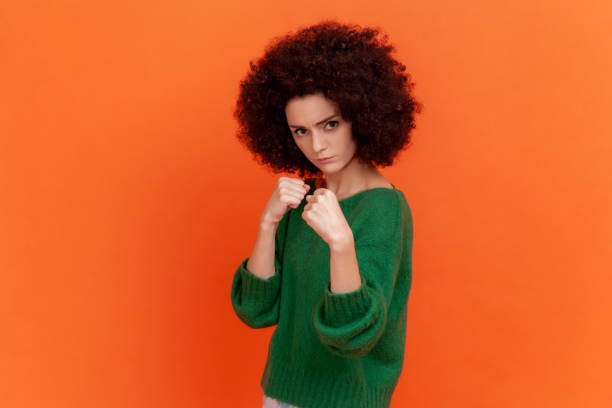 retrato de mujer agresiva con peinado afro con suéter verde de estilo casual de pie con los puños levantados listo para pelear, boxeando. - serious punching fighting displeased fotografías e imágenes de stock