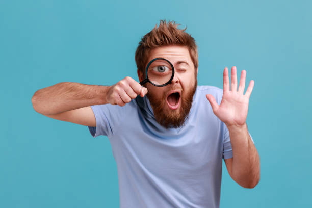 man holding magnifying glass and looking at camera with big zoom eye, waving hand, saying hi. - huge eyes imagens e fotografias de stock