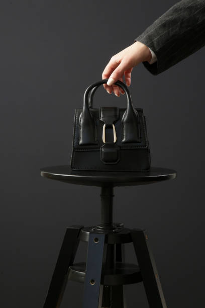 Top handle mini black bag made in textured, resistant leather. Studio shot on black background.