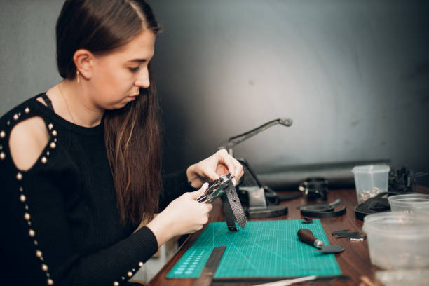 Tanner woman making leather harness belt goods on workshop. Working process of leather craftsman.
