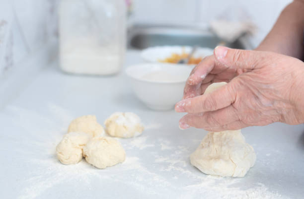 istock Senior woman hands form blanks for pies on a white kitchen table with blurred grated apple and sugar on background. Selective focus. Process of making pies with apple filling. Cooking at home concept 1392636360