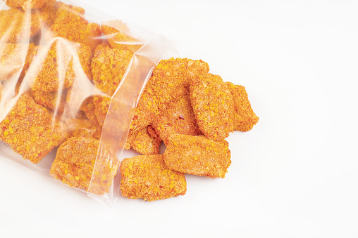 Breaded chicken nuggets. Semifinished. Fast cooking.Frozen breaded nuggets fillet pieces in a transparent bag on an isolated background.Fast food, food at home.