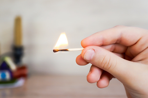 the child holds a lit match and it burns with a flame.