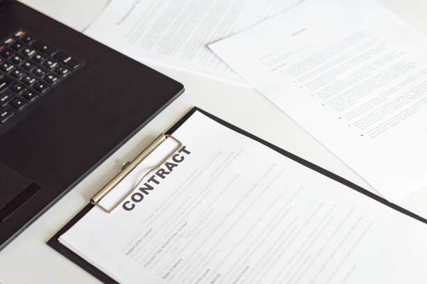 istock Side view of contract in clipboard lying at office on table with laptop and documents 1392637383