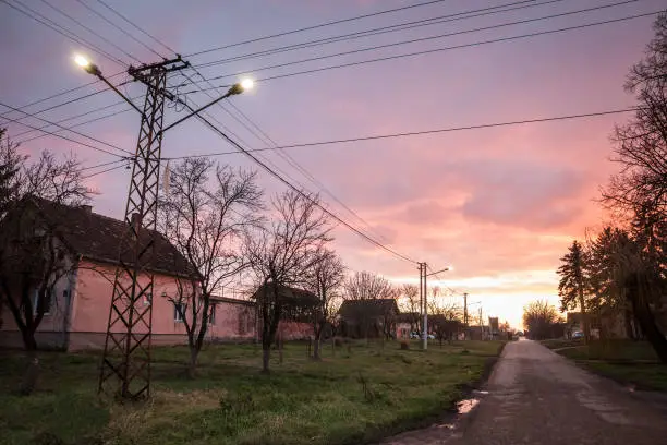 Photo of Selective blur on an old pylon of a power electric line and a Street Lamp light, with an old connection system to the public network of electricity in the neglected village of banatsko Novo selo, Serbia.