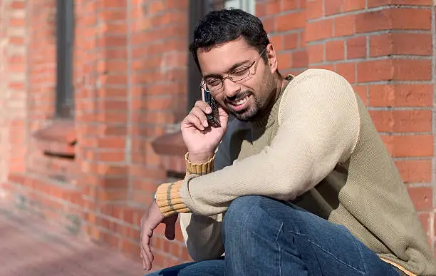 an indian man talking on a cell phone. sharpness is on the man - the background is blurred with lenses.
