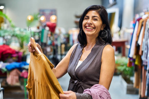 une travailleuse latino-américaine triant des vêtements dans un magasin de vêtements - boutique store owner latin american and hispanic ethnicity photos et images de collection