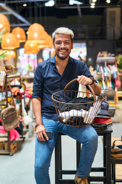 ouvrière latino-américaine assise dans un magasin de vêtements tenant un panier plein d’écharpe - boutique store owner latin american and hispanic ethnicity photos et images de collection