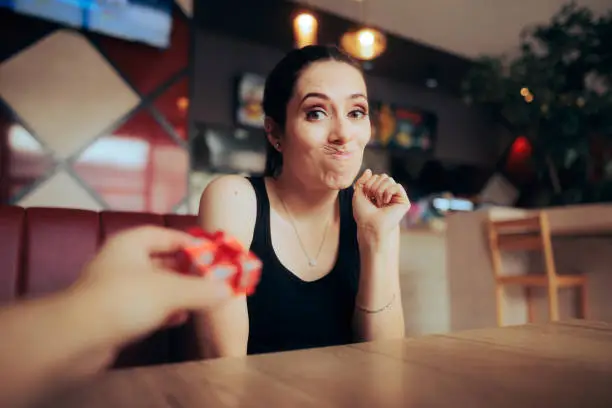 Photo of Surprised Girlfriend Reluctant to Accept a Small Gift from her Date
