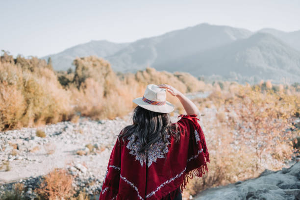 traditionelle lateinamerikanische frau mit einem roten poncho und einem hut von hinten gesehen, in einem natürlichen raum. stärkung der rolle der frau - ecuadorian culture stock-fotos und bilder