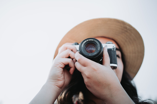 Close up. Summer vibe young female digital nomad wearing a hat and using a vintage camera to take photos in a natural space. High quality photo. Copy space